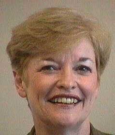 Close-up portrait of a smiling person with short blond hair against a plain background