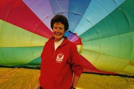 Woman in a red jacket standing in front of a colorful hot air balloon envelope