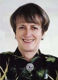 Portrait of a smiling person in a dark patterned blouse with a round pendant necklace on a light background