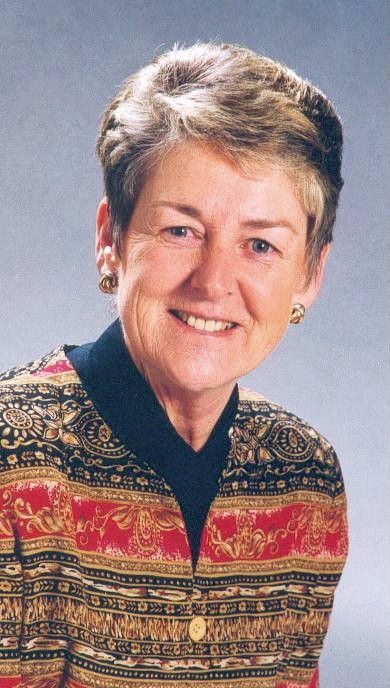 Portrait of a smiling person in a patterned red, black, and gold sweater on a gray background