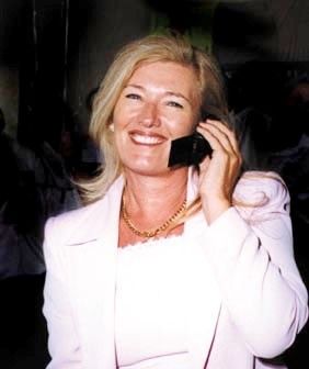 Smiling woman in a white blazer holding a phone to her ear in a dark setting