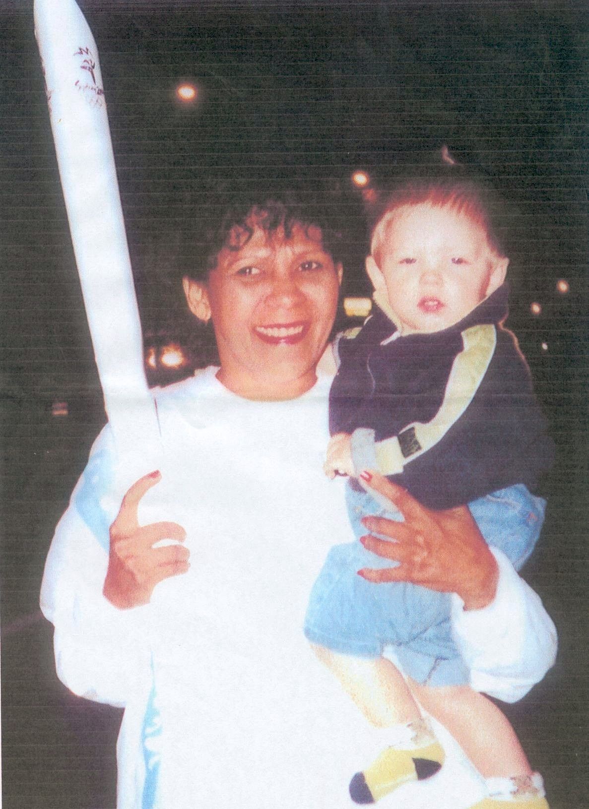 Adult holding a smiling child at night, with bright lights in the background.
