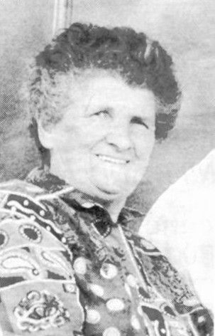 Smiling woman in a patterned blouse, seated and facing slightly to the right.