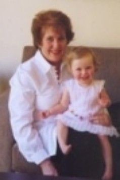 Woman seated on a couch holding a smiling child in a white dress