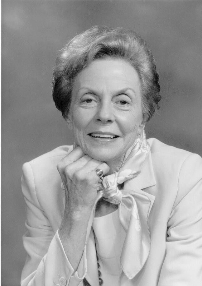 Portrait of a smiling woman in a light suit with a bow, resting her chin on her hand.