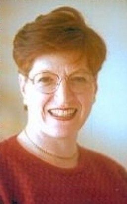 Smiling person with short reddish hair and glasses wearing a red top against a light background