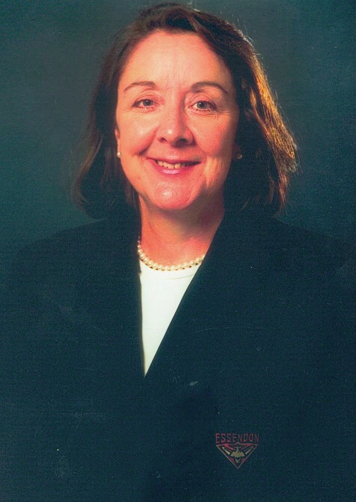 Studio portrait of a smiling woman in a dark blazer against a teal background