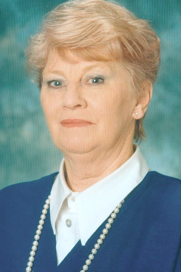 Studio portrait of a woman in a blue blazer, white blouse, and pearl necklace against a teal backdrop