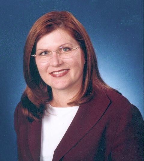 Smiling person with glasses in a maroon blazer against a blue studio background