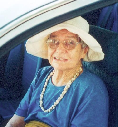 Woman wearing a white sunhat and glasses, seated in a car and smiling at the camera