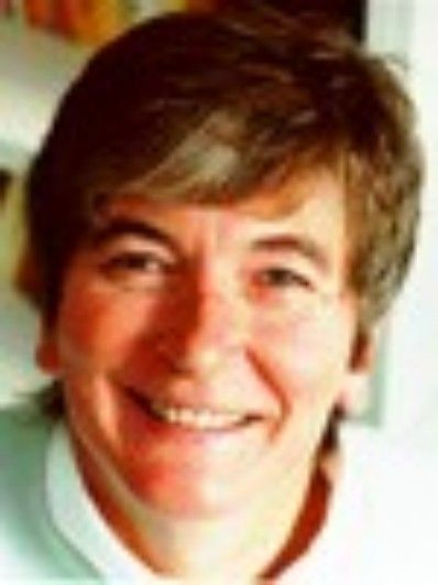 Smiling person with short brown hair, wearing a white collared shirt, against a neutral background