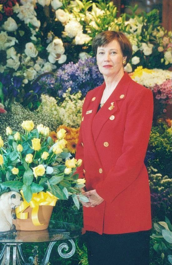Woman in a red blazer standing beside a bouquet display of white and yellow flowers