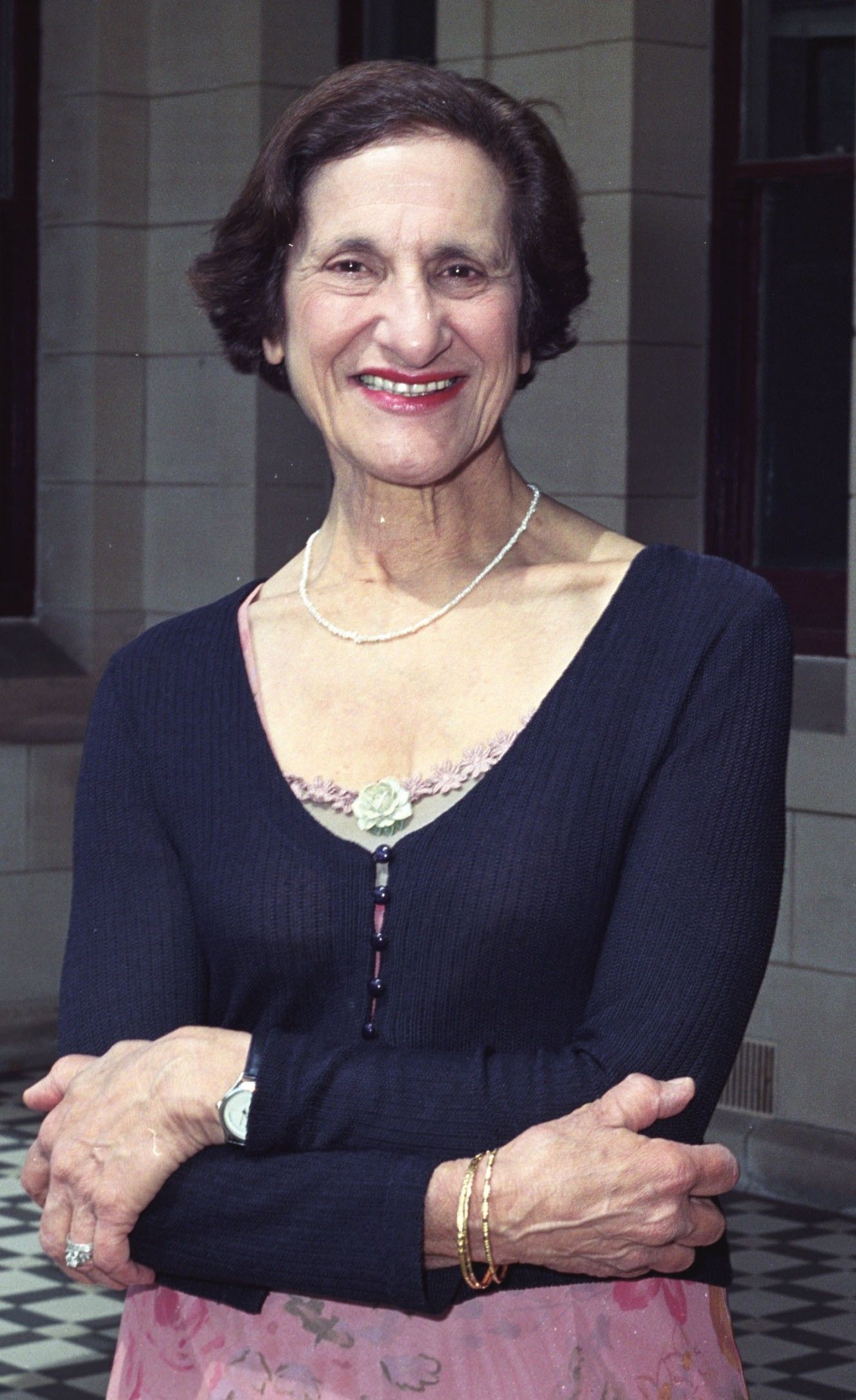 Smiling woman in a dark top, seated with folded arms against a stone building backdrop.