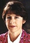 Portrait of a woman with short dark hair, wearing a pink polka-dot blouse and white collar, on a dark background