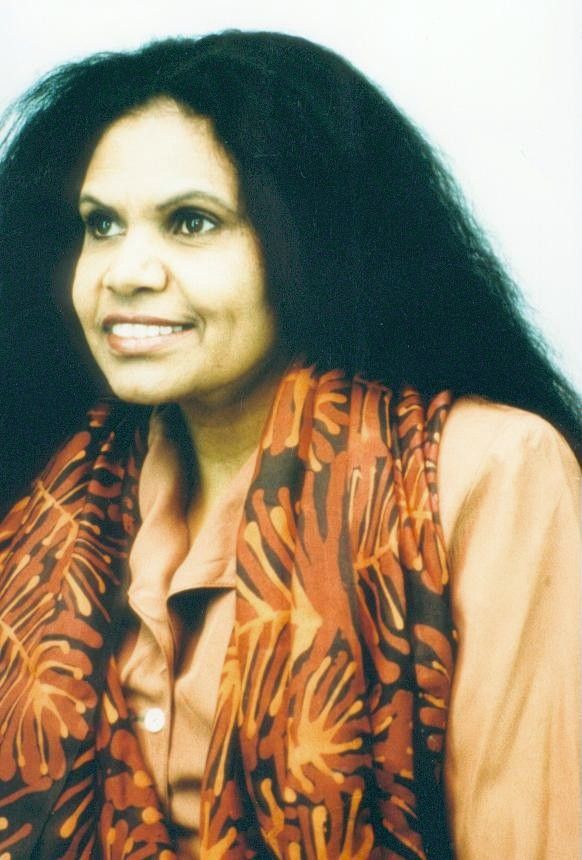 Smiling woman with long dark hair, wearing an orange patterned scarf against a light background