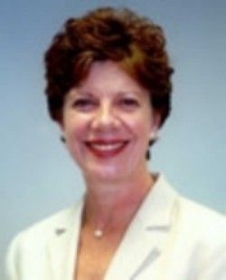 Smiling woman in a white blazer against a light blue background