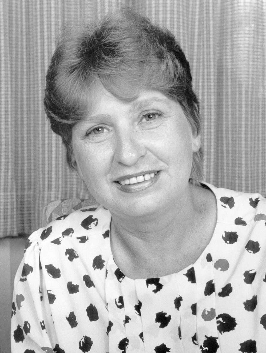 Smiling woman in a patterned blouse, seated against a striped backdrop.