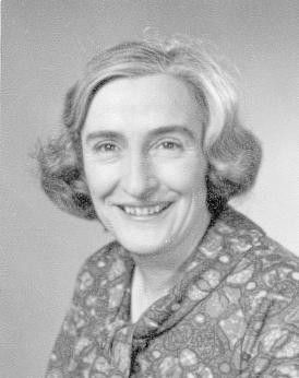 Black-and-white portrait of a smiling woman with short wavy hair in a patterned blouse.