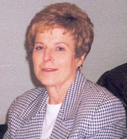 Portrait of a woman with short light brown hair in a plaid blazer, seated indoors