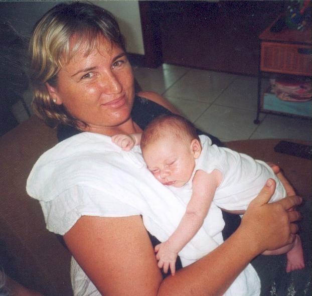 Woman holding a sleeping baby in a living room, both dressed in white.