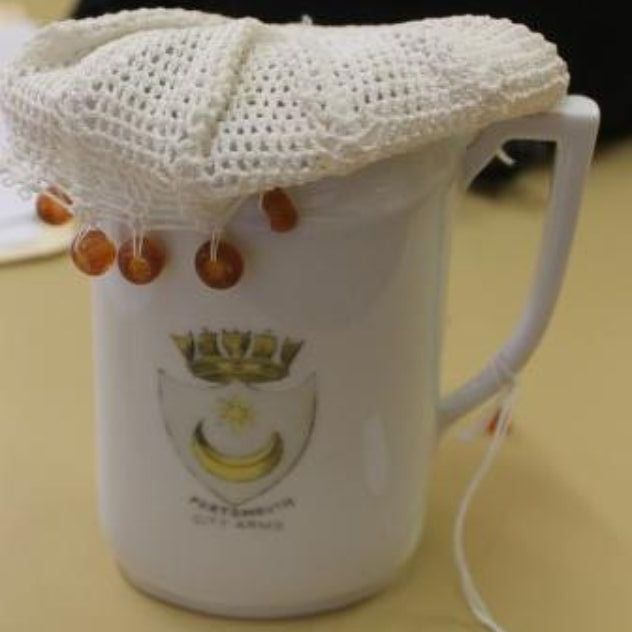 White mug with a lace cover and dangling beads on a table