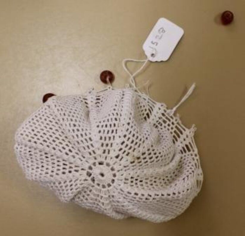 White crocheted drawstring pouch on beige surface with a small price tag attached