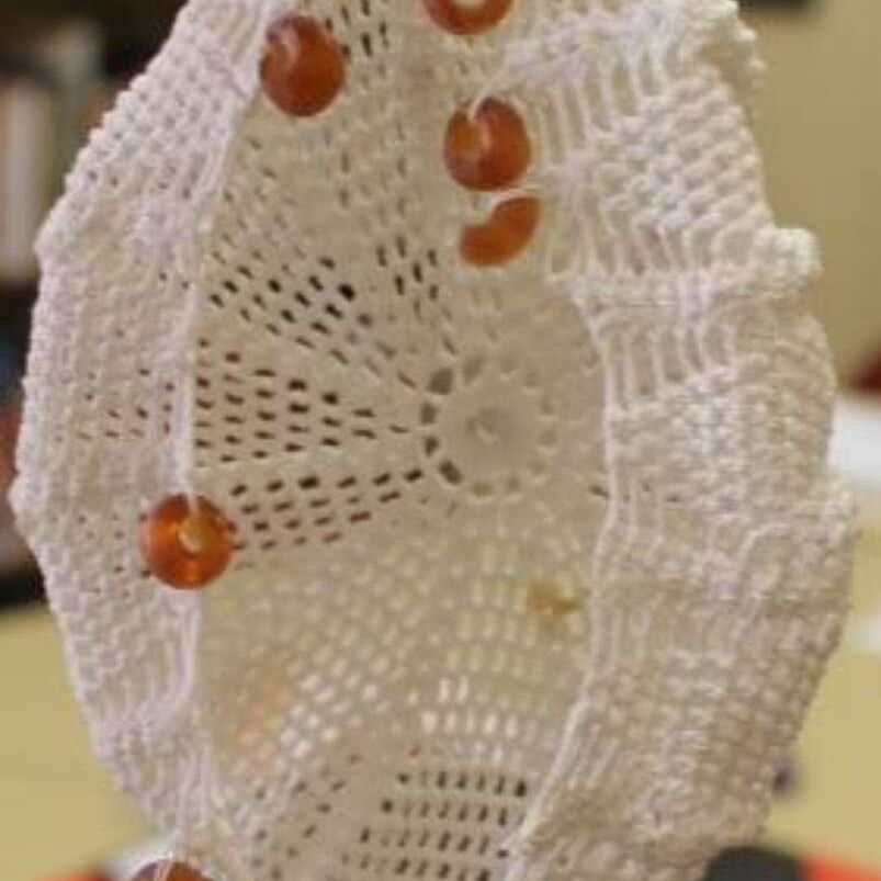 White crochet doily with several amber beads, hanging against a blurred background.