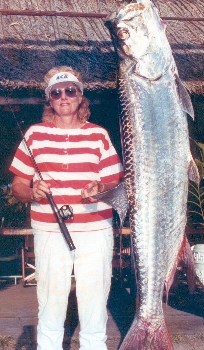 Person in red-striped shirt and white pants standing beside a large hanging fish.