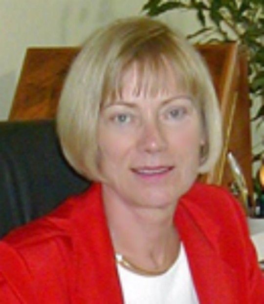 Woman in a red blazer seated in an office chair, looking at the camera.
