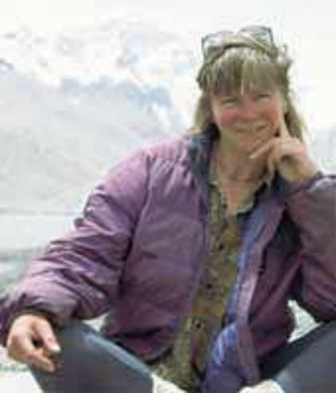 Woman in a purple jacket smiling outdoors by a snowy mountain lake