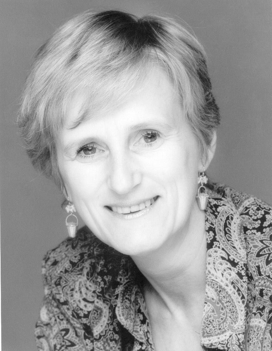 Smiling woman with short hair in a patterned blouse, posed against a plain gray background