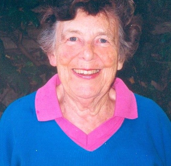 Smiling woman in a blue sweater with a pink collar against a dark background
