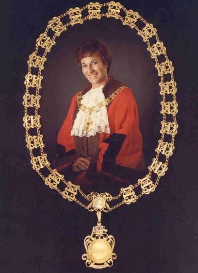 Portrait of a smiling person in a red and black outfit, framed by an ornate gold oval necklace.