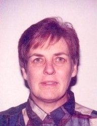 Portrait of a person with short brown hair wearing a plaid shirt, facing forward against a plain background