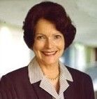Smiling woman with short dark hair wearing a maroon blazer and striped shirt, posed indoors.