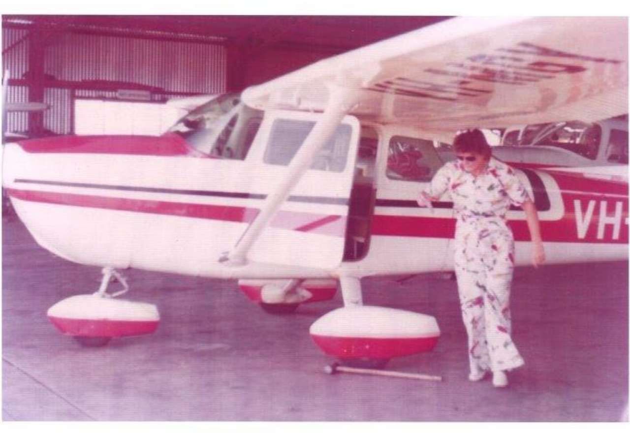 Small white-and-red airplane in a hangar, with a person standing by the wing and landing gear.