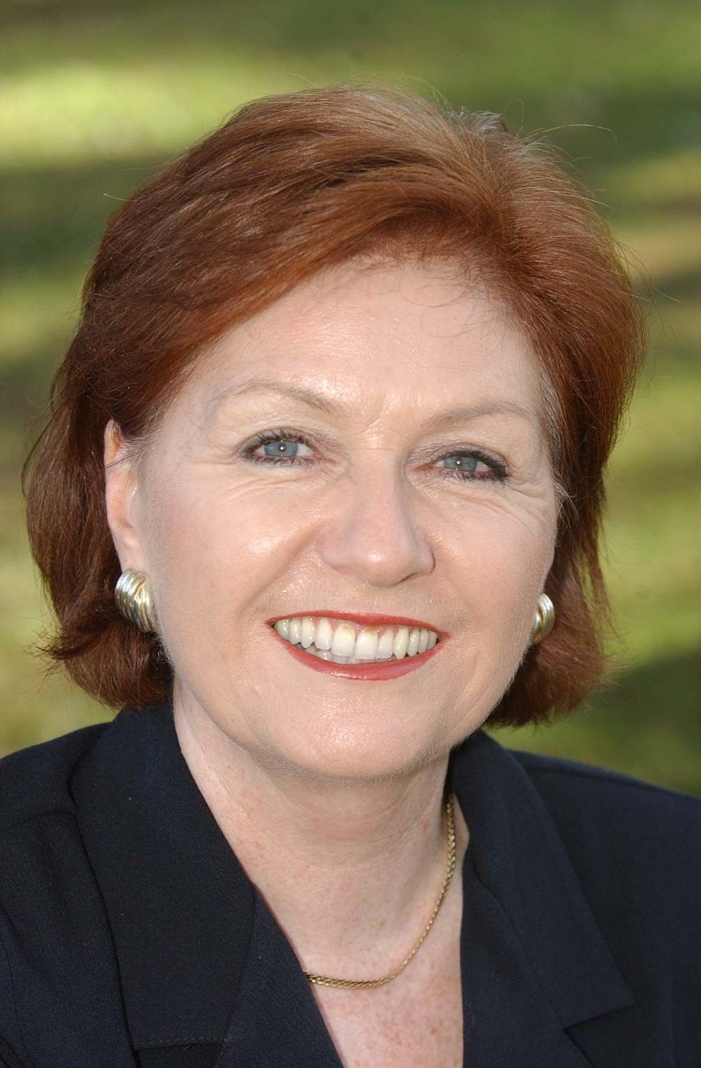 Smiling woman with short auburn hair in a dark blazer against a blurred green background