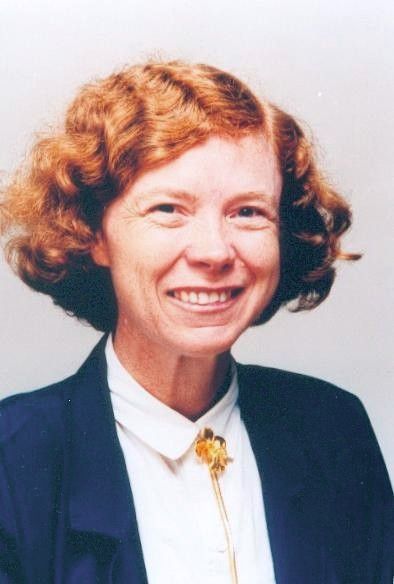 Portrait of a smiling woman in a navy jacket and white blouse with a gold floral brooch