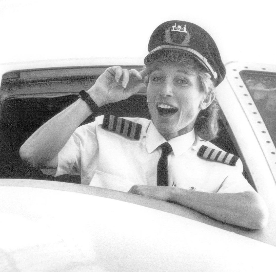 Pilot smiling and saluting from an airplane cockpit, wearing a cap and uniform