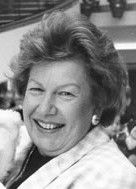 Smiling woman in a black-and-white portrait, wearing a light jacket and earrings