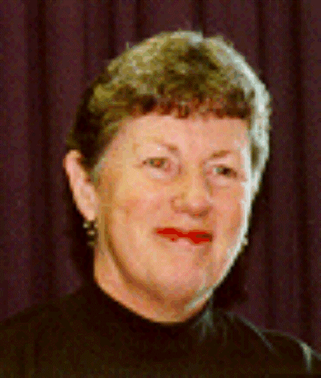 Portrait of a smiling person in a dark turtleneck, standing before a burgundy curtain.