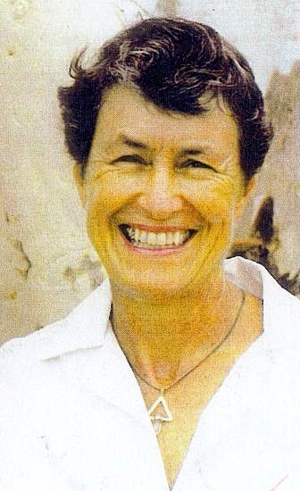 Smiling person in a white shirt and triangular necklace against a light background