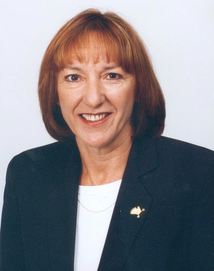 Studio headshot of a smiling woman in a dark blazer and white top on a light background