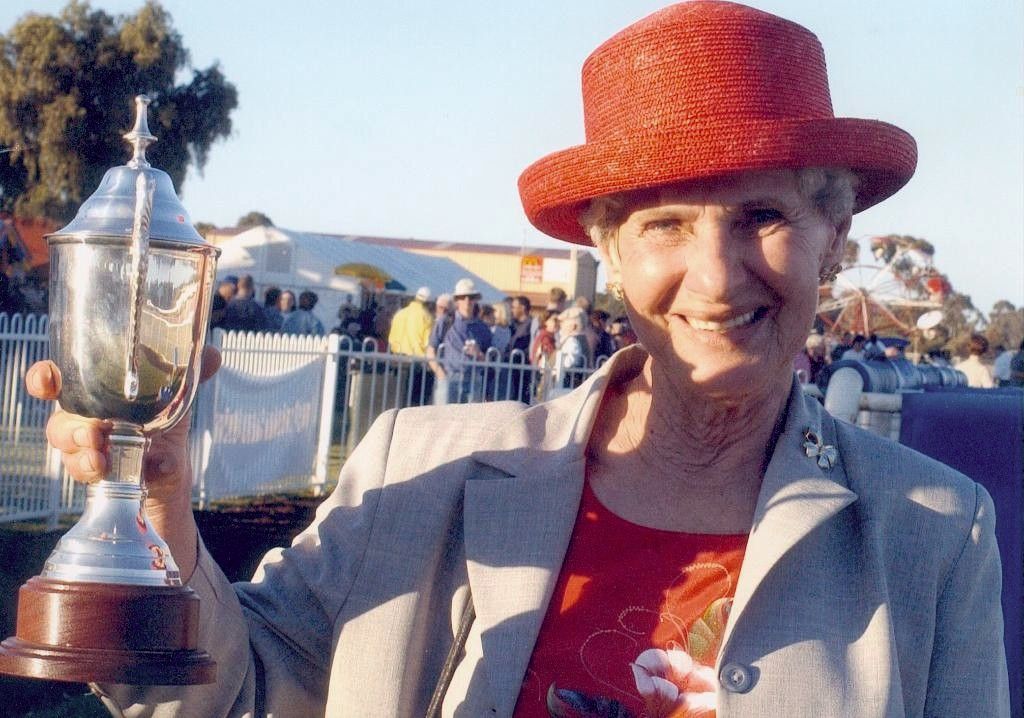 Smiling person in a red hat holding a trophy outdoors at a crowd-filled event