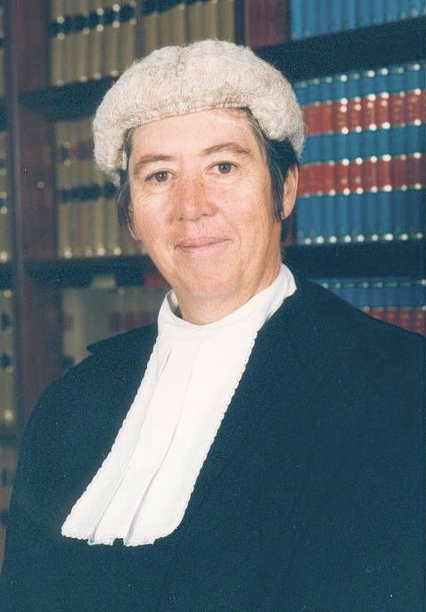 Portrait of a judge in a white wig and robe, standing before shelves of law books