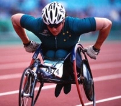 Paralympic cyclist in teal racing on a track, leaning forward in a handcycle with a white helmet.