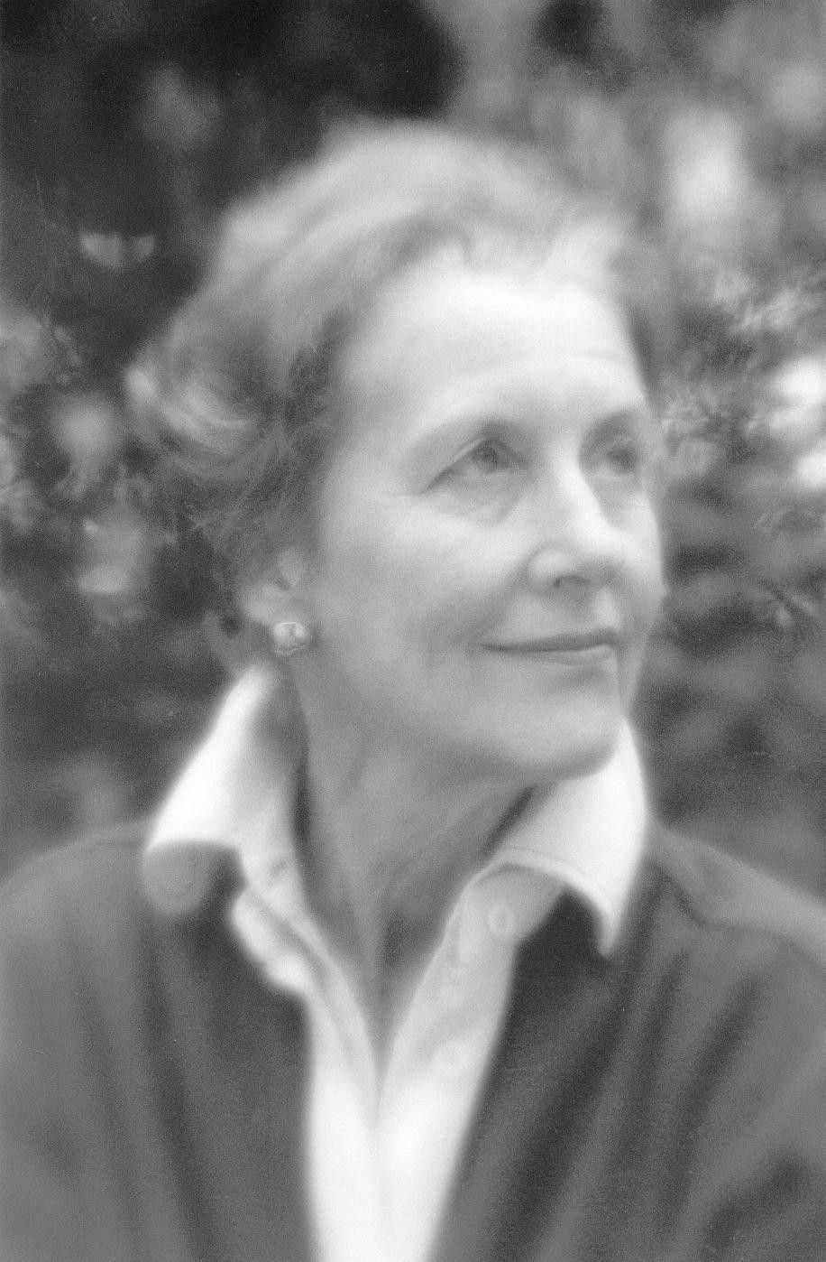 Portrait of a person in a collared shirt and sweater, looking off to the side against a blurred outdoor background