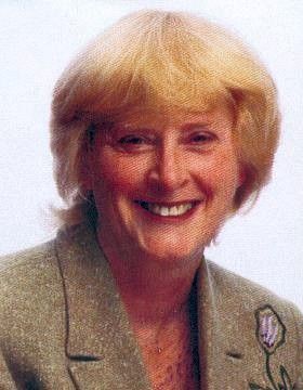Smiling woman with short blond hair in a light blazer against a plain background