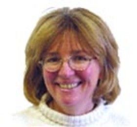 Smiling person with glasses and shoulder-length hair wearing a white turtleneck on a white background