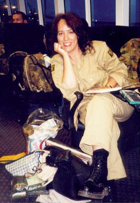 Woman in beige outfit reclining on a chair, smiling in a dim room with bags at her feet.